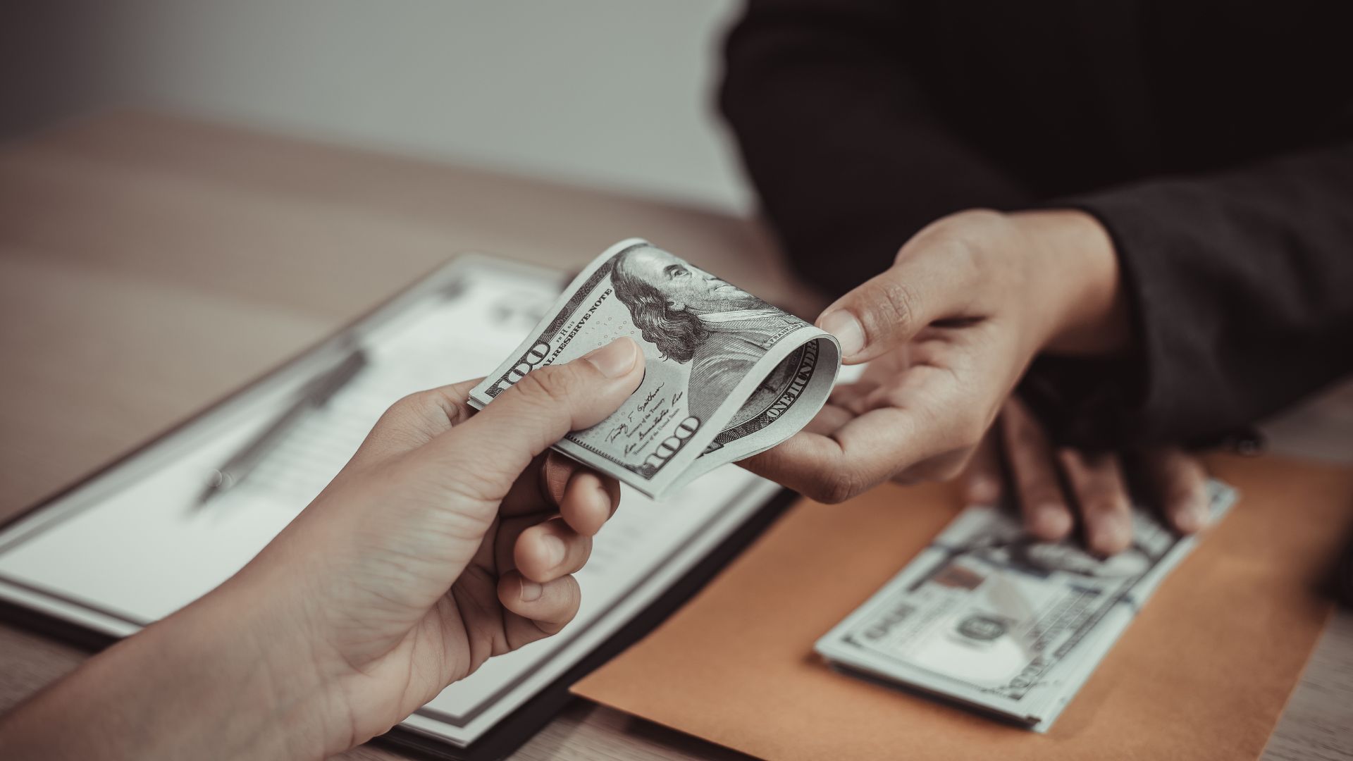 a person handing a roll of cash across a table to to another person