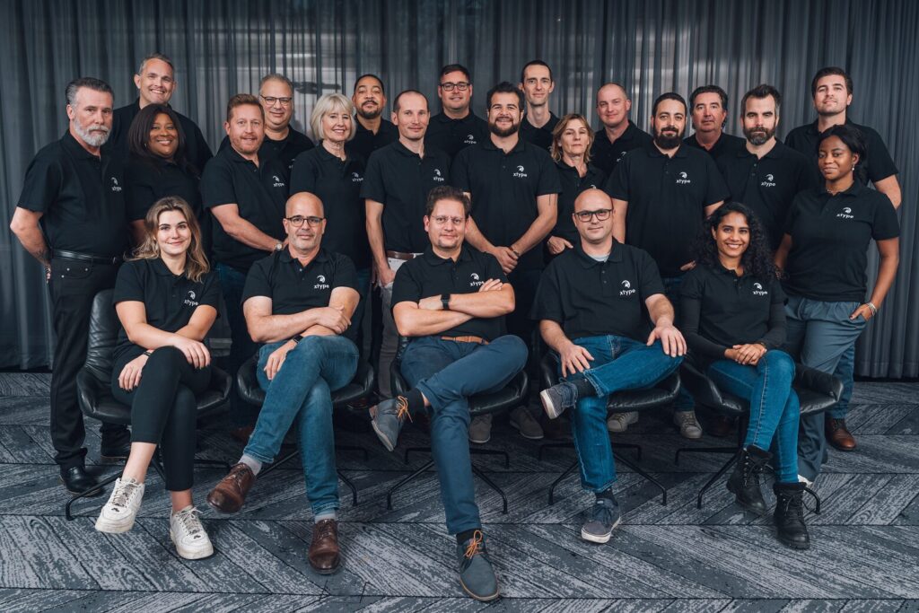 a photo of the xtype team where 23 employees wearing black polos pose for the camera