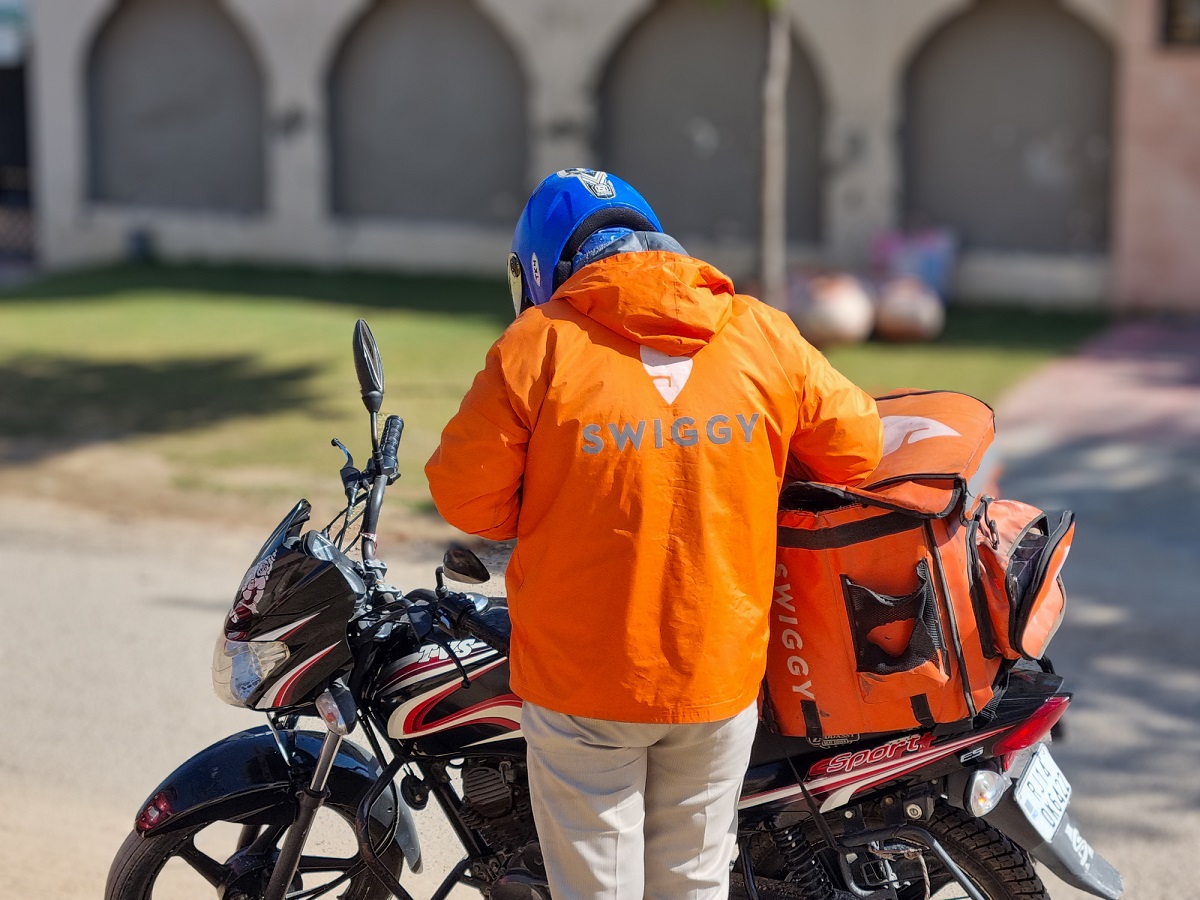 A Swiggy delivery driver standing by a motorcycle