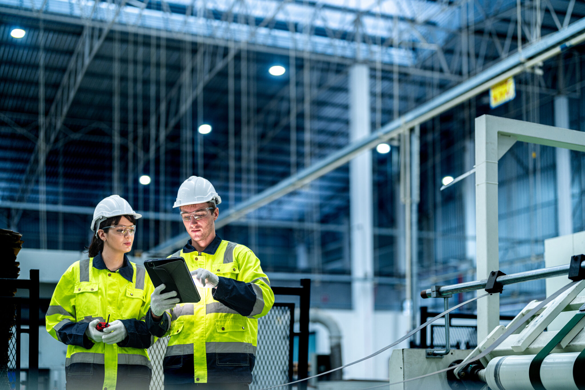 two techs wearing hardhats in an industrial setting looking at a tablet